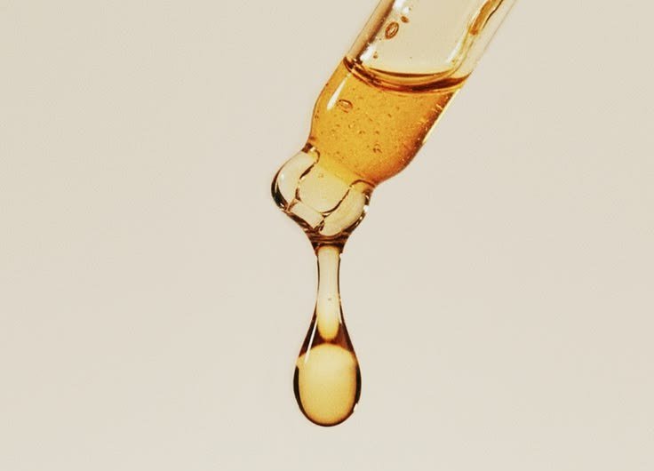 Gotero de vidrio cargado de aceite dorado, con una gota a punto de caer