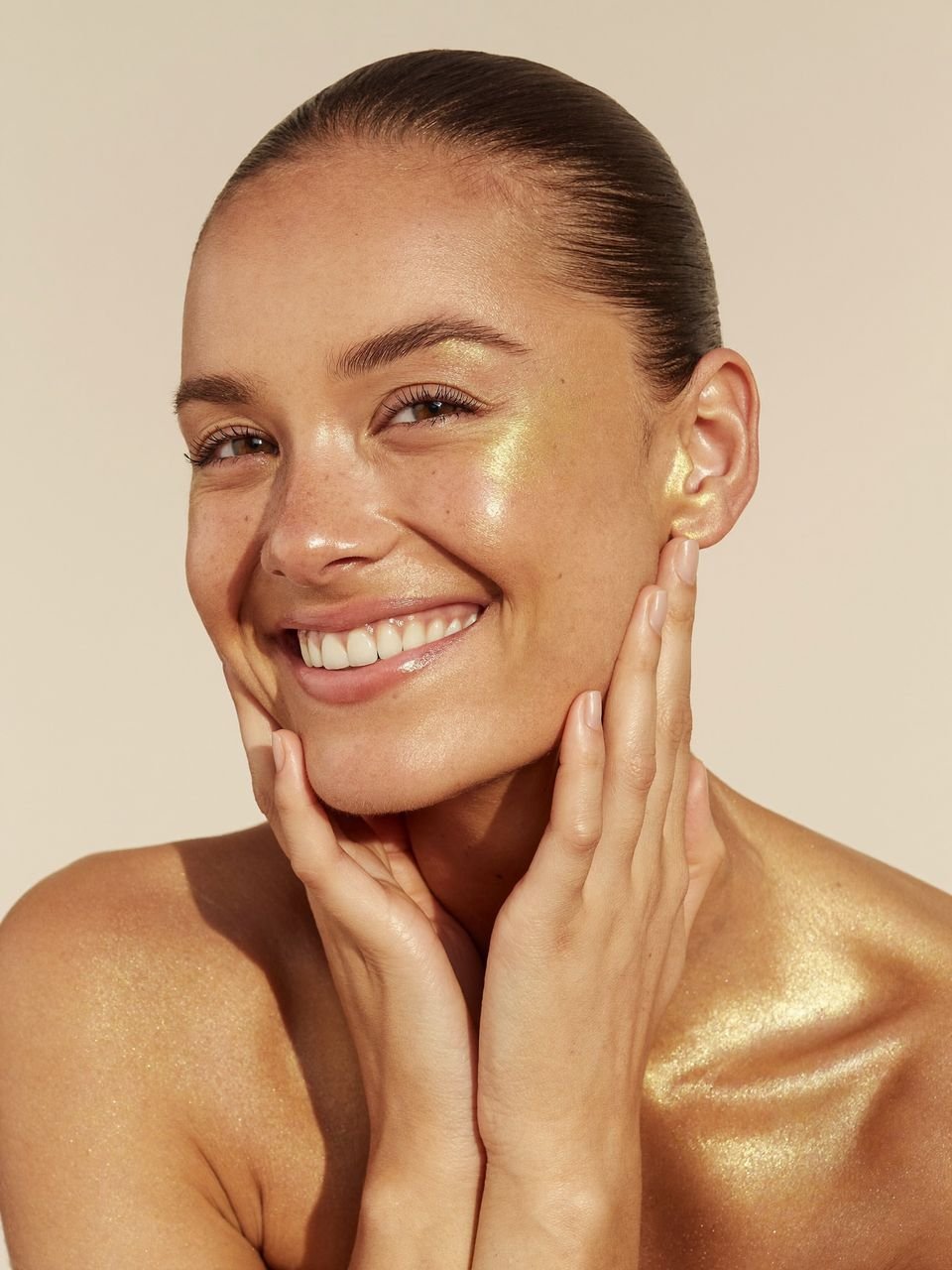 Mujer sonriendo con las manos junto al rostro y la piel luminosa