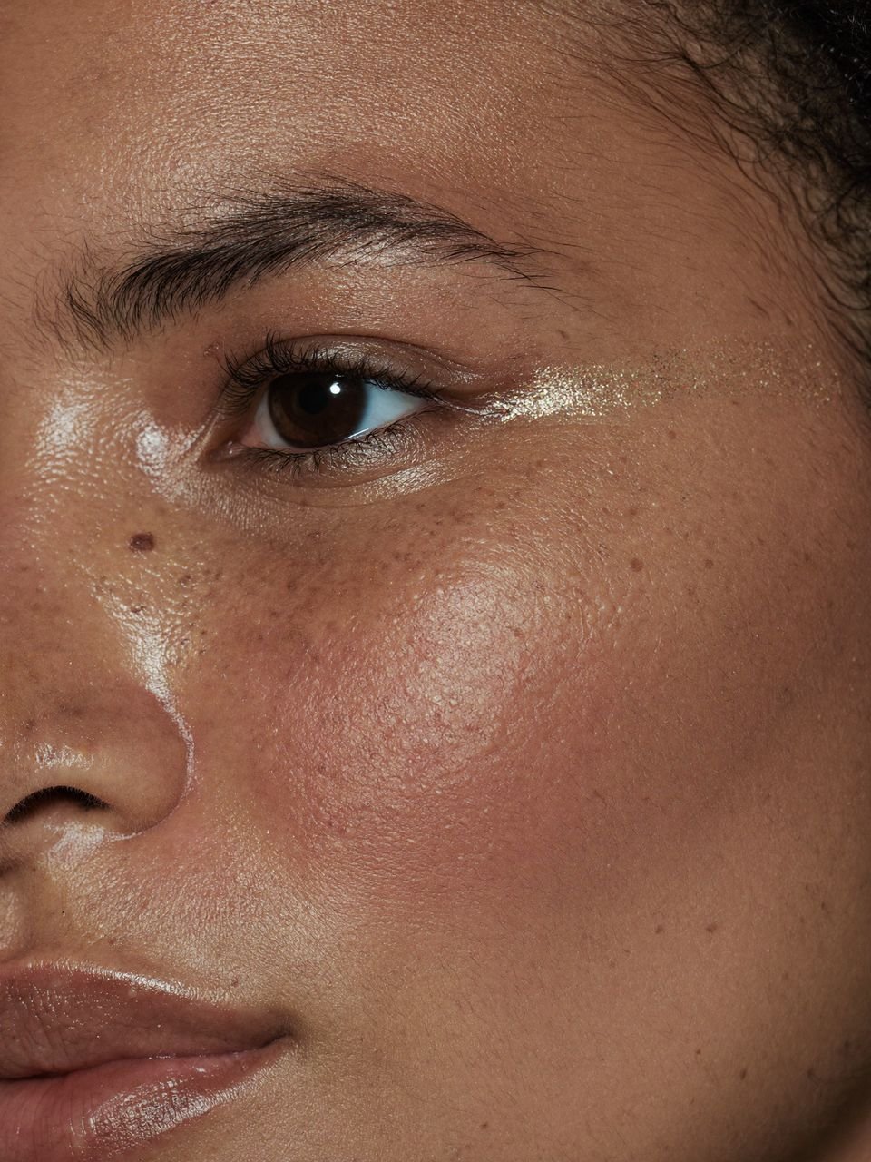 Primer plano de un ojo y la mejilla con pecas y destellos dorados sobre la piel